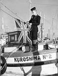 A Canadian sailor prepares to hoist the Union Jack on the expropriated Japanese-Canadian fishing boat KUROSHIMA NO.2, New Westminster, British Columbia, Canada, 29 December 1941 Deember 29, 1941