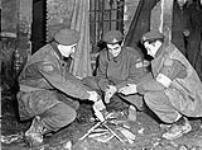 Privates Dougal, M. Guerette and A. Corneau, all of the Royal 22e Régiment, warming their hands around a small fire, Ravenna, Italy, 10 February 1945 February 10, 1945
