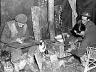 Gunners George Blagdon and Frank Klein and Sergeant Leonard Tremblay, all of the Royal Canadian Artillery (R.C.A.), making a stove from a 4.5-inch shell charge case, Ravenna, Italy, 10 February 1945 February 10, 1945