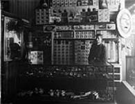 Interior of a tobacco shop, with the tobacconist leaning on the counter. Display cases have a nice assortment of clay, meershaum, and briar pipes, as well as various cigars, cigar sundries, and some cigarettes ca. 1905