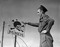 Able Seaman Douglas F. Trewin, W-2 Party, Royal Canadian Navy Beach Commando "W", points out a Able Seaman Douglas F. Trewin, W-2 Party, Royal Canadian Navy Beach Commando "W", points out a German sign warning of mines in the Juno sector of the Normandy beachhead, France, 20 July 1944 20-Jul-44