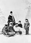 Harriot Georgina, comtesse de Dufferin, et membres de sa famille photographiés dans un décor d'hiver de studio avec un toboggan, un traîneau et des raquettes à neige 1873