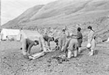 [Left to right: Harold Kalluk, Gedeon Qitsualik, Daniel Komangaapik, Uirngut, Paul Idlout and Rebecca Qillaq Idlout. Joseph Idlout is seen in front bending over. They were cutting up a seal.] 1951
