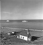 "Mission catholique romaine, vue aérienne de l'église avec le NGCC C.D. Howe ancré à l'arrière-plan, Pond Inlet (Mittimatalik/Tununiq), Nunavut, juillet 1951 " July 1951.