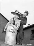 An unidentified airman attempts to put the lid on a garbage can which contains a man dressed as Adolf Hitler, No.1 Bombing and Gunnery School (B.G.S.) (Royal Canadian Airforce Schools and Training Units), Royal Canadian Airforce (R.C.A.F), Jarvis, Ontario, Canada, July 1941 July, 1941.