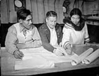 Alex Stevenson, du ministère des Ressources et du Développement économique, et officier responsable de la patrouille de l'Est de l'Arctique, se faisant informer du naufrage d'un navire par des agents de sureté inuits de la GRC qui se dirigent vers le poste de Craig Harbour, T.N.-O. [Nunavut], à bord du CGS C.D. HOWE, juillet 1951 [De gauche a droite: Joe Panikpakoochoo, Alex Stevenson, et Panikpak]. juillet 1951.