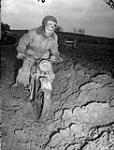Trooper Allan Hemphill, a despatch rider with Headquarters Squadron, Governor General's Foot Guards, rides his motorcycle through a muddy field south of Udem, Germany, 26 February 1945 February 26, 1945.
