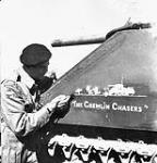 Lieutenant R.H. Heggie putting the finishing touches on "The Gremlin Chasers" painting on his Sherman tank of the Three Rivers Regiment near Lucera, Italy, 21 October 1943 October 21, 1943.
