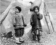 [Inuuk children, Jayko Tunrak, and Enoya Shooyook, in front of a tent with a sealskin float hanging on the front] [Two Inuit children in front of a sealskin float hanging on a tent]. Original title: Eskimo child in front of sealskin tent at Arctic Bay n.d.
