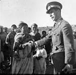 Cst. Van Blazcom shakes hands with an Inuit woman on a Belcher Island [Caroline Novalinga (child standing behind Cst. Van Blazcom's outstretched arm) and Shovia Eyatiuk (woman standing behind the child looking at Cst. Van Blazcom)] 1949.