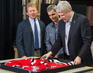 [Prime Minister Stephen Harper, joined by Rick Dykstra, frames a hockey jersey at Framecraft ltd. with help from Joe Mancino, owner of Framecraft ltd. in St. Catharines, Ontario] 22 January 2015