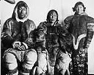 [C/Cst. Tululick "Scottie", Tululick's wife, and their daughter Tutuucktuuck "Koo-tuck-tuck"] wearing caribou parkas posing in front a cloth March 1905.