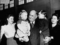 Honourable Humphrey Mitchell, Minister of Labour, welcomes two displaced persons children in Reception Centre at Saint-Paul-l'Ermite, on their arrival in Canada from Germany Jan. 1948.