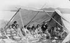 A group of Tsimshian people having a tea party in a tent, Lax Kw'alaams (formerly Port Simpson), B.C., c. 1890 c. 1890.