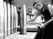 Male worker inspects Bren gun shells on table in Canadian munitions plant Dec. 1939