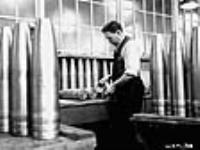 Male munitions worker measuring shells as part of testing process Dec. 1939