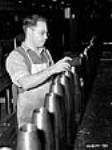 Male munitions worker measuring shells as part of testing process Dec. 1939