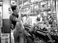 Male machinist in a Canadian Bren gun factory peers down bore of barrel to detect flaws déc. 1939
