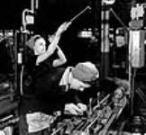 À l'usine de fusils-mitrailleurs Bren, la John Inglis Co., une femme vérifie l'intérieur d'un canon de ce type d'arme pendant qu'une autre règle une machine pour percer le tube de ce même modèle de fusil 8 Apr. 1941