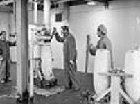 Des ouvriers portant des appareils respiratoires se préparent à remplir une bombe avec des matériaux prévus à cet effet à l'usine Cherrier mai 1941