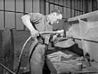 A workman operates an emery grinder on a profiled propeller blade at the Canadian Propeller Co Mar. 1942