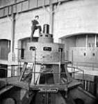 L'employé William Patrick Smith se tient debout sur la génératrice no 5 à l'intérieur de la centrale Chute-à-Caron, lors de l'aménagement hydroélectrique de Shipshaw Jan. 1943