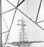 Des ouvriers en haut d'un poteau raccordent les lignes de transmission des circuits 11 et 12 lors du projet d'aménagement hydroélectrique de Shipshaw Jan. 1943