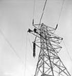 Workmen for the sub-contractor Hoosier Co., fix an insulator into position on an electricity transmission tower during construction of the Shipshaw power plant Jan. 1943