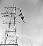 Workmen for the sub-contractor Hoosier Co., fix an insulator into position on an electricity transmission tower during construction of the Shipshaw power plant Jan. 1943