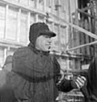 Jules Legresley, aide-poseur de rivets, a pour fonction de maintenir la barre à rivets pendant que le poseur de rivets fixe la barre en place; aménagement hydroélectrique de Shipshaw Jan. 1943