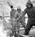 Driller Phillip Rousseau thaws out his drill in the fire during the Shipshaw Power Development project janv. 1943