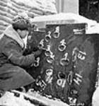 Un ouvrier mesure le trou produit dans une tôle au cours d'un tir d'essaide munitions aux bancs d'essai de Valcartier févr. 1943