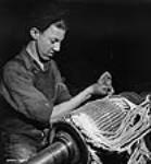 Dans l'atelier de l'Alcan Aluminium Limitée d'Arvida, Marcel Rhéaume, aide-installateur d'enroulements, enlève l'enroulement de l'induit janv. 1943
