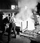 Workmen throw an electrolytic sheet of zinc into a melting furnace at the Consolidated Mining & Smelting Company of Canada Ltd Apr. 1943