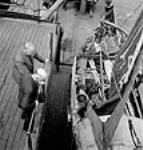 Male inspectors look on while a trial run crewman strips a life-boat during the test run of a new cargo ship juil. 1943