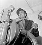 Quartermaster Edmond Belodeau of Levis, Quebec, holds the wheel of a new cargo freighter during its test run juil. 1943