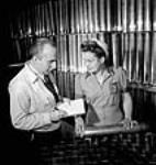 Former interior decorator Harold Webster takes notes from former waitress Nettie Dowbush, both now employed at the Dominion Bridge Company's munitions plant, Harold Webster as an editor for the D.B. News plant publication and Nettie Dowbush as a hydraulic press operator déc. 1943