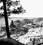 Vue du campement du lac Steep Rock avec son puits de mine abortif, ses bureaux d'affaires, ses dortoirs, le remblai et le barrage pendant le développement d'une mine à ciel ouvert Jan. 1944