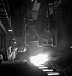 Un ouvrier prélève de l'acier en fusion d'un four à creuset ouvert pour le couler dans des moules et en faire des lingots à la Stelco Steel Company of Canada 1944