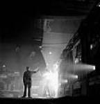 À l'usine de la société Stelco Steel Company of Canada, un ouvrier dirigela coulée d'acier en fusion d'une poche de coulée au four à creuset ouvert mars 1944