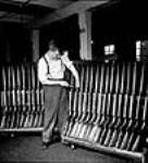 Workman Dave Carr inspects and numbers .22 calibre training rifles in the H.W. Cooey Company Ltd. munitions plant mai 1944