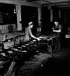 Female and male worker Georgina Jacobson (left) and William Lingard oil and pack .22 calibre training rifles for shipment at the H.W. Cooey Company Ltd. munitions plant May 1944