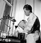 Un employé passe une solution d'amberlite dans un entonnoir de filtrationpour obtenir une solution finale de sel de sodium débarrassée de son excédent de sel aux laboratoires Connaught May 1944