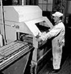 Aux usines Cherrier et Bouchard de la société Defense Industries Limited,l'ouvrier F.H. Joubert applique un couche de peinture sur un obus pour l'empêcher de rouiller juil. 1944