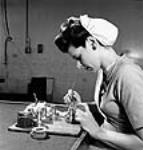 L'ouvrière Margot Bourassa applique du vernis à la gomme-laque sur le corps d'une fusée dans la salle de broyage de l'usine Cherrier de la société Defense Industries Limited juil. 1944