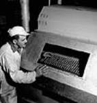 Worker F.H. Joubert coats a shell case to prevent rust in the Cherrier and Bouchard plants of the Defense Industries Limited July 1944