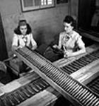 Female workers Claire Briere (left) and Pauline Chartbrand weigh the completed 20 m.m. shell in the government inspection line at the Cherrier or Bouchard plants of the Defence Industries Limited juil. 1944