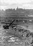 Vue de la plus grande pelle mécanique canadienne chargeant un train de minerai d'amiante dans une mine à ciel ouvert, la mine Jeffrey, exploitée par la société Johns-Mainville Canada Inc juin 1944