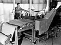 À l'usine Johns-Manville à Asbestos (Québec), Armand Jutras conduit une machine à onduler d'épaisses feuilles de papier d'amiante utilisées pour entourer les  tuyaux June 1944