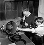 Le lieutenant Schubert Fraser et M. John DeGrott essaient un mégaphone utilisé par la marine à l'usine RCA Victor July 1944